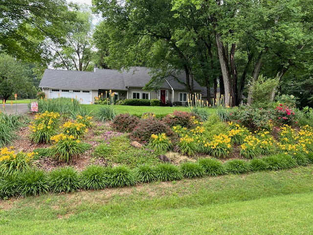 A house sits behind a beautiful yard full of colorful flowers and bushes.