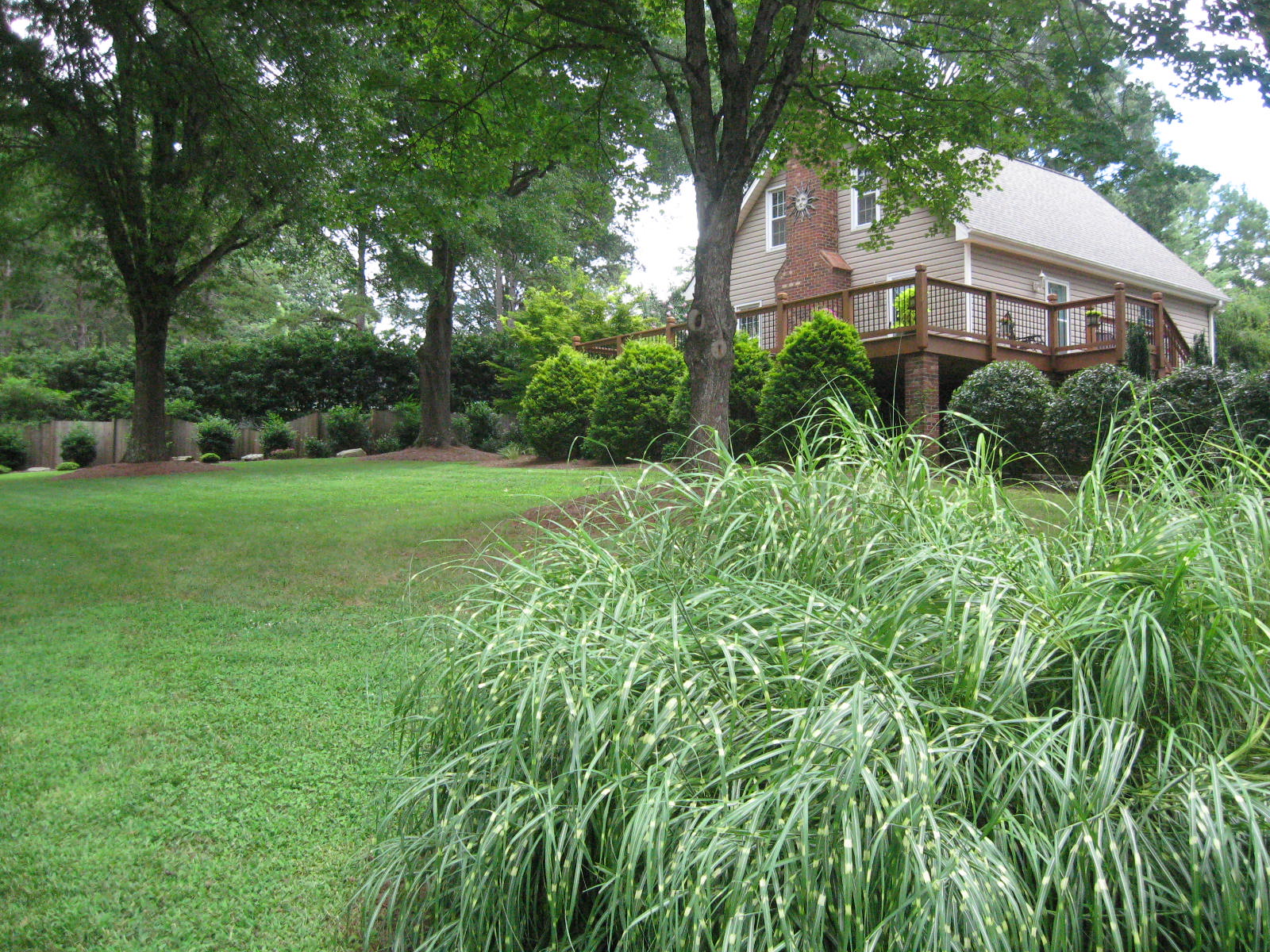 A manicured lawn surrounds a stunning beige home with a wooden deck