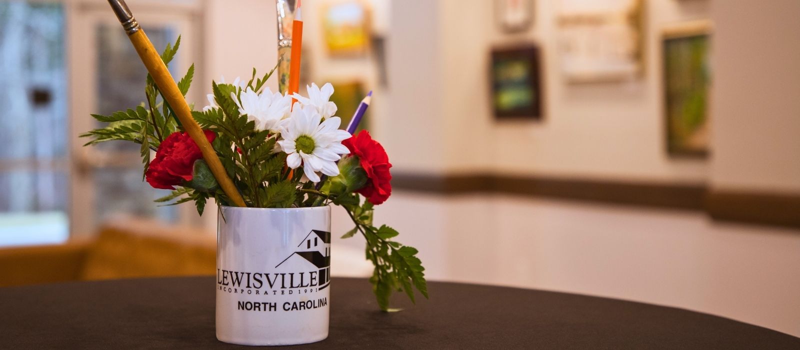 Art show display with a Lewisville mug and flowers