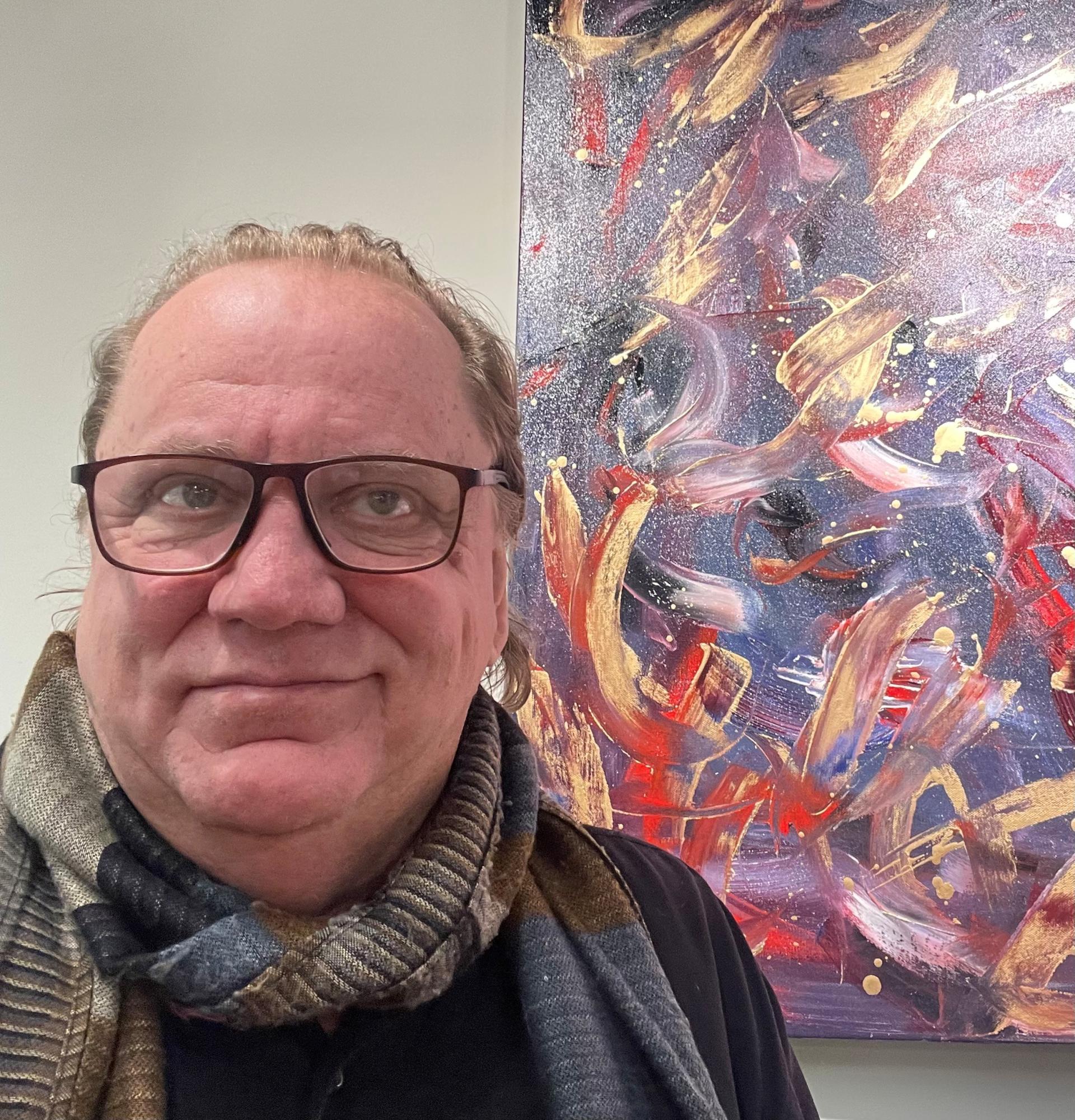 A man wearing glasses and a scarf stands close to a colorful abstract painting.