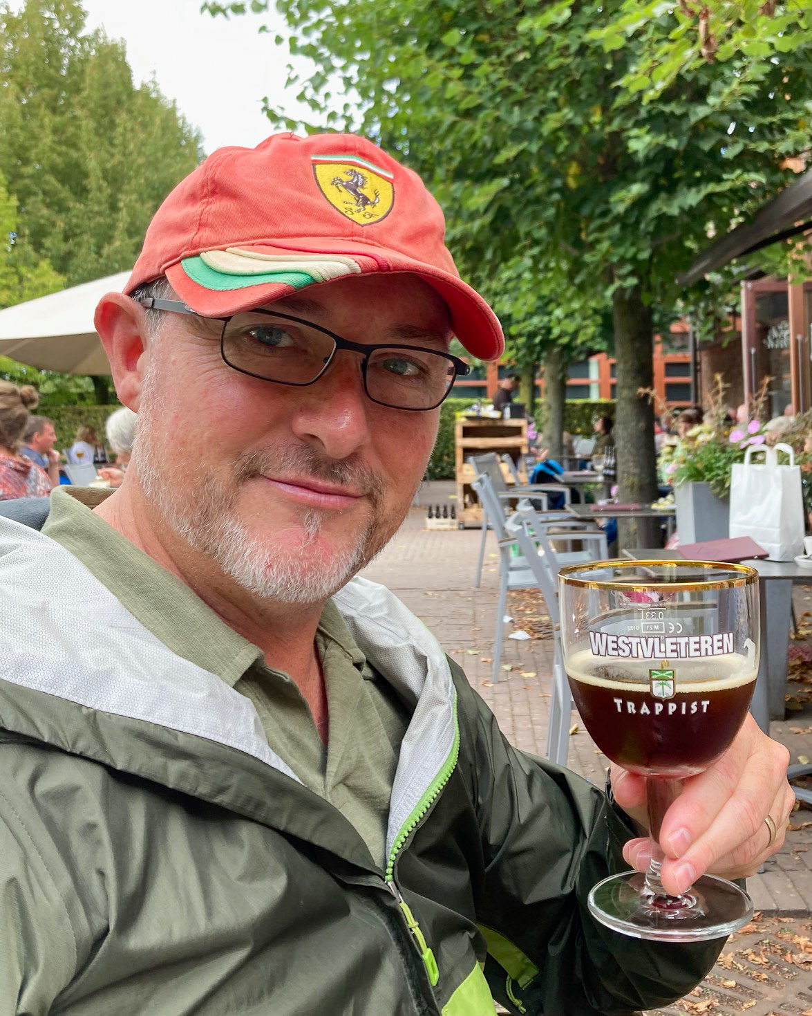 Man in a red hat and green jacket smiles while holding a glass
